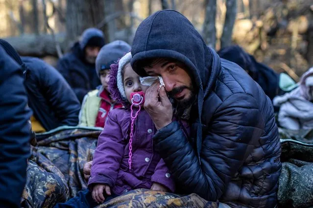A man holding a child reacts as the members of the Kurdish family from Dohuk in Iraq wait for the border guard patrol, near Narewka, Poland, near the Polish-Belarus border on November 9, 2021. The three-generation family of 16 members with seven minors, including the youngest who is five months old, spent about 20 days in the forest and was pushed back to Belarus eight times. They claim they were beaten and frightened with dogs by Belarusian soldiers. (Photo by Wojtek Radwanski/AFP Photo)