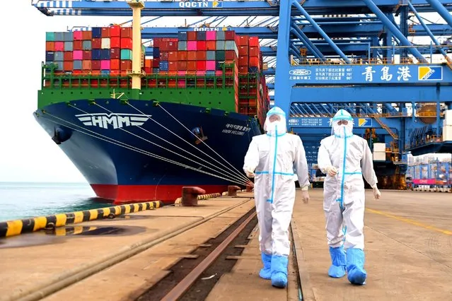 China immigration inspection officers in protective overalls march near a container ship at a port in Qingdao in eastern China's Shandong province Sunday, November 7, 2021. China's exports remained strong in October, a positive sign for an economy trying to weather power shortages and COVID-19 outbreaks.(Photo by Chinatopix via AP Photo)