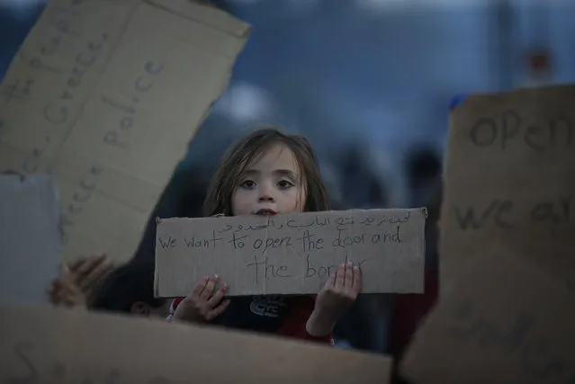 A migrant girl holds a banner, during protest in the make shift refugee camp, at the northern Greek border point of Idomeni, in Greece, Saturday, March 19, 2016. (Photo by Darko Vojinovic/AP Photo)
