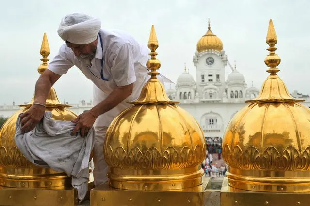 A Sikh volunteer of the Guru Nanak Nishkam Sewak Jatha (GNNSJ), a faith-based charitable organisation cleans gold platings at the Golden Temple in Amritsar on March 28, 2024. (Photo by Narinder Nanu/AFP Photo)