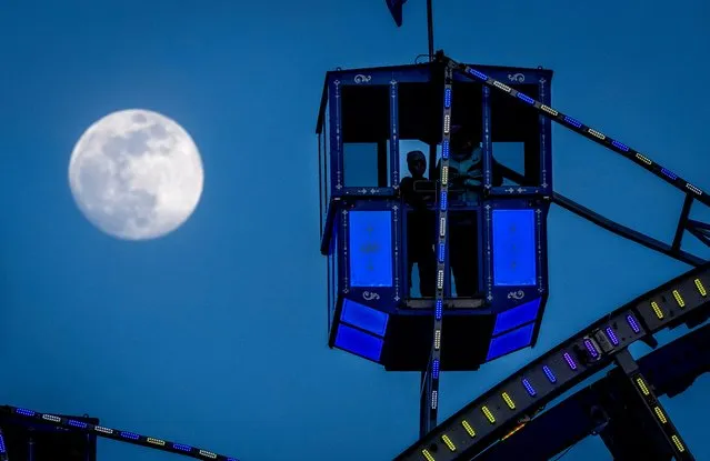 The moon rises next to a gondola of a ferris wheel on the spring fun fair in Frankfurt, Germany, Saturday, March 23, 2024. (Photo by Michael Probst/AP Photo)