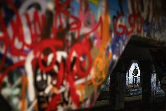 A person rides a scooter through the Krog Street Tunnel in Atlanta, Friday, June 28, 2019. The tunnel runs under train tracks carrying freight cars and is known for its urban street art. Connecting the eclectic neighborhoods of Cabbagetown and Inman Park, the tunnel also serves as a message board with frequently updated posts about local events and shows. (Photo by David Goldman/AP Photo)