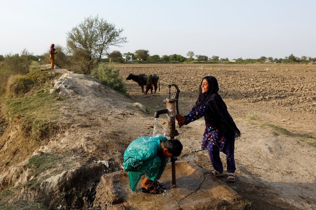 A girl uses a handpump as a boy cools off from the water drawn from it during a hot summer day as a heatwave continues, in Jacobabad, Pakistan on May 24, 2024. (Photo by Akhtar Soomro/Reuters)