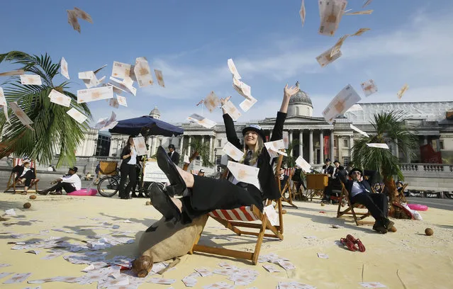 A protestor throws fake money into the air as she relaxes on a deckchair in an interactive, tropical tax haven beach in Trafalgar Square in London, Thursday, May 12, 2016. MPs and members of the public will be invited to have their photograph taken at the beach, to support Oxfam, Action Aid and Christian Aid's call to end tax havens. The charities have organised the interactive stunt to coincide with the Government's international Anti Corruption Summit which takes place at nearby Lancaster House on Thursday. (Photo by Kirsty Wigglesworth/AP Photo)