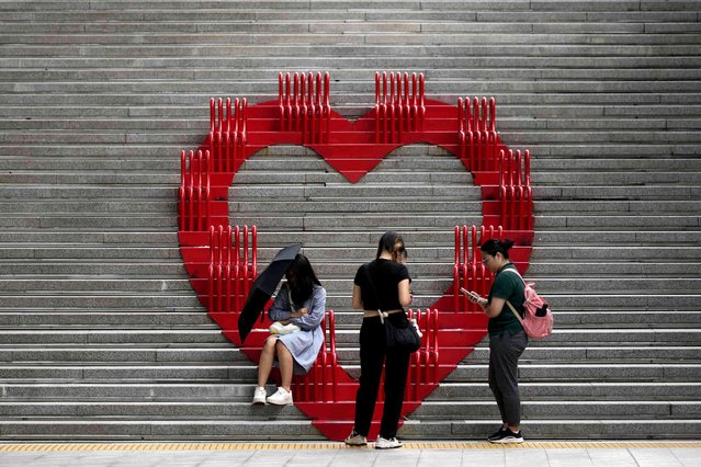 A visitor shades herself from the sun with an umbrella as others look their smartphones in Seoul, South Korea, Wednesday, July 10, 2024. (Photo by Lee Jin-man/AP Photo)