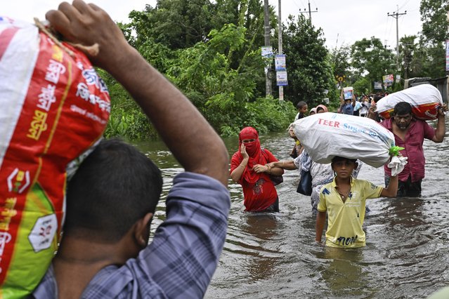 People walk to a relief shelter with belongings through a flooded street following heavy rains in Mohipal, Feni, a coastal district in southeast Bangladesh, Friday, August 23, 2024. (Photo by Fatima Tuj Johora/AP Photo)