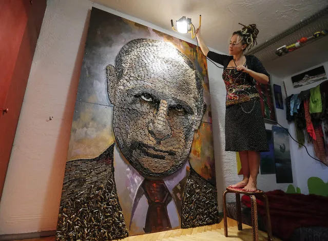 Ukrainian artist Daria Marchenko lights up her artwork “The Face of War” which depicts Russian President Vladimir Putin in Kiev, Ukraine, 05 August 2015. “The Face of War” – is the first picture in the series “Five Elements of War” which Daria Marchenko plans to create. About 5,000 cartridge cases of different calibres for different types of weapons from the eastern Ukrainian conflict zone were used for creating of this artwork. (Photo by Roman Pilipey/EPA)