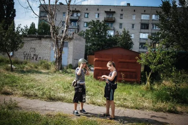 A boy wearing a military helmet sits with his friend near a camp of Ukrainian battalion “Donbass”, which is based in school, during relocation one of the parts from battalion “Donbass” in the eastern Ukrainian town Popasnaya, in Ukraine, 04 August 2014. A group of international experts managed to reach the Malaysia Airlines plane believed to have been shot down on 17 July by pro-Russian separatists in Ukraine. (Photo by Roman Pilipey/EPA)