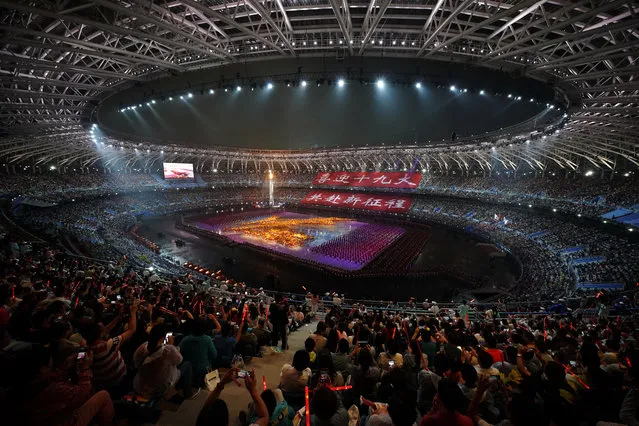 Spectators watch performers dance on stage with huge red banners reads “Welcome the 19th Party Congress, go to a new journey together” during the opening ceremony of the 13rd National Games in north China's Tianjin Municipality on Sunday, August 27, 2017. (Photo by Chinatopix via AP Photo)