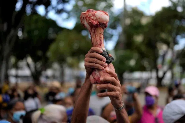 A protester holds up a bone to refer to hunger during a demonstration by active and retired public workers, including teachers, demanding better salaries and the rest of their vacation bonus which they say was paid partially, as they march to the Labor Ministry in Caracas, Venezuela, Tuesday, August 2, 2022. (Photo by Ariana Cubillos/AP Photo)