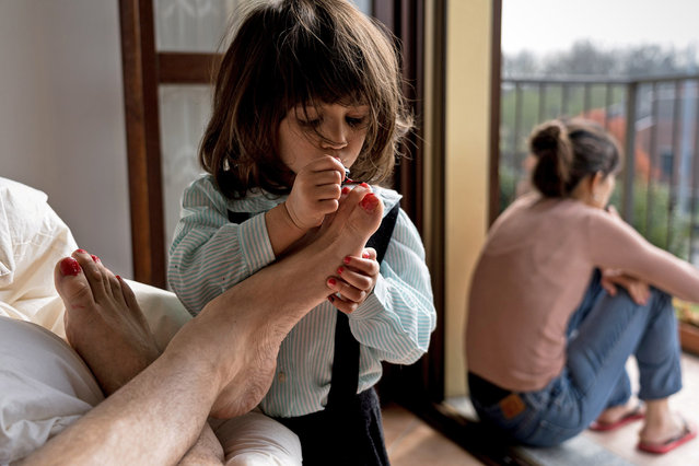 Life in lockdown: Schoolteacher Marzio Toniolo, 35, takes a picture of his two-year-old daughter Bianca painting his toenails as they while away time at home in San Fiorano, one of the original “red zone” towns in northern Italy that has now been extended to the whole country, as his wife, Bianca's mum Chiara Zuddas looks out from their balcony, March 20, 2020. Toniolo has been documenting how his family has dealt with being under quarantine since it began for them in February. (Photo by Marzio Toniolo via Reuters)
