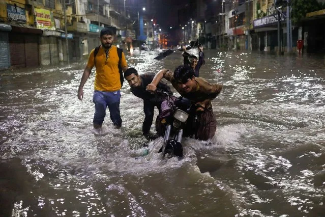 Boys push their motorcycle after it was stopped on a flooded street, following heavy rains during the monsoon season in Karachi, Pakistan on July 24, 2022. (Photo by Akhtar Soomro/Reuters)