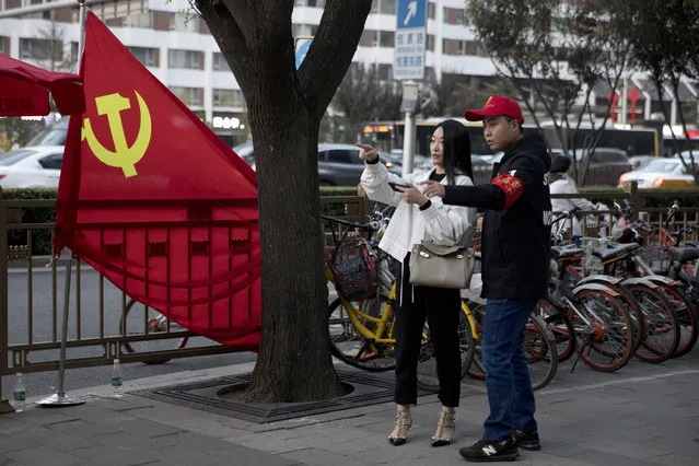 In this October 16, 2017 photo, a deputized citizen gives direction to a resident near a Chinese Community Party flag on the streets of Beijing, China. (Photo by Ng Han Guan/AP Photo)