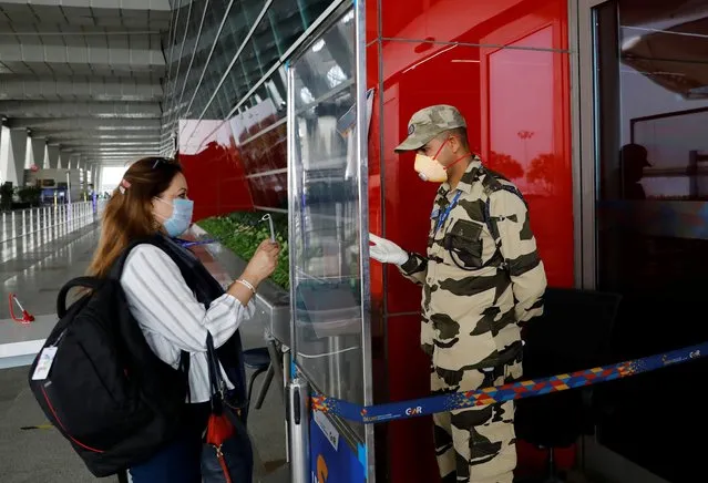 A member of the Central Industrial Security Force (CISF) checks the ID of a woman through a glass shield, after the government allowed domestic flight services to resume from coming Monday, during an extended nationwide lockdown to slow the spread of the coronavirus disease (COVID-19), at the Indira Gandhi International (IGI) Airport, in New Delhi, India, May 23, 2020. (Photo by Anushree Fadnavis/Reuters)