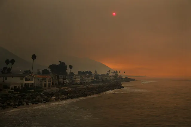 Homes stand along the beach as the sun is visible through thick smoke from a wildfire Wednesday, December 6, 2017, in Ventura, Calif. A dramatic new wildfire erupted in Los Angeles early Wednesday as firefighters battled three other destructive blazes across Southern California. (Photo by Jae C. Hong/AP Photo)