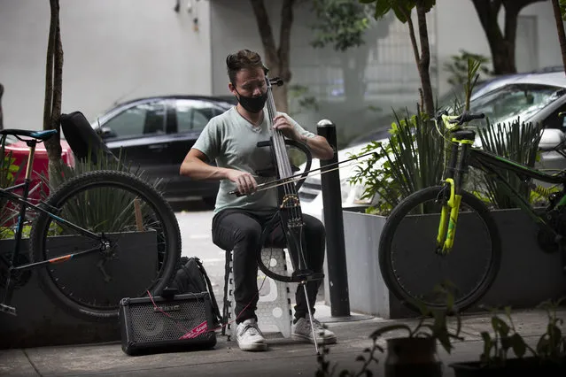 A musician, wearing a protective face mask as a precaution against the spread of the new coronavirus, plays his cello outside the Pizzeria Zaza, in Mexico City, Saturday, August 15, 2020. The government of Mexico City has allowed bars to operate as restaurants that began Monday in order to reopen as part of an easing of the new coronavirus lockdown. (Photo by Marco Ugarte/AP Photo)