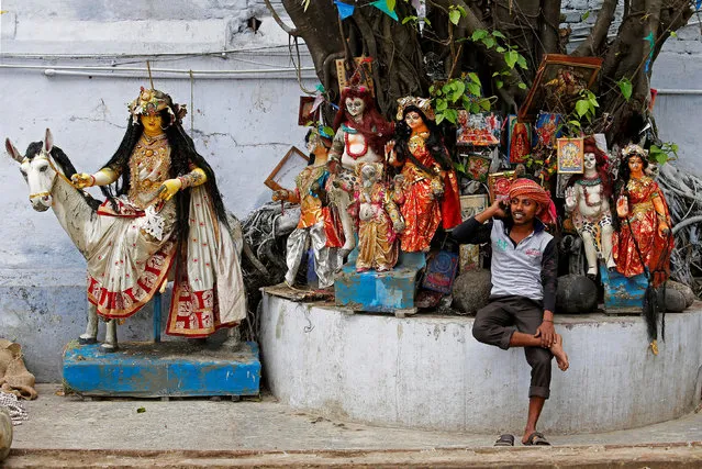 A labourer speaks on his mobile phone as he takes rest in front of idols of Hindu deities which are kept under a tree at a market area in Kolkata, India, April 2, 2018. (Photo by Rupak De Chowdhuri/Reuters)