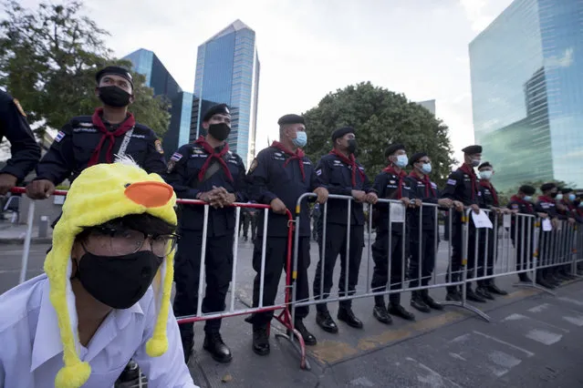 A protester wearing a headgear designed as a yellow duck, which has become a good-humored symbol of resistance during anti-government rallies, sits in front of police standing guard outside the Siam Commercial Bank Wednesday, November 25, 2020 in Bangkok, Thailand. Thai authorities have escalated their legal battle against the students leading pro-democracy protests, charging 12 of them with violating a harsh law against defaming the monarchy. (Photo by Wason Wanichakorn/AP Photo)