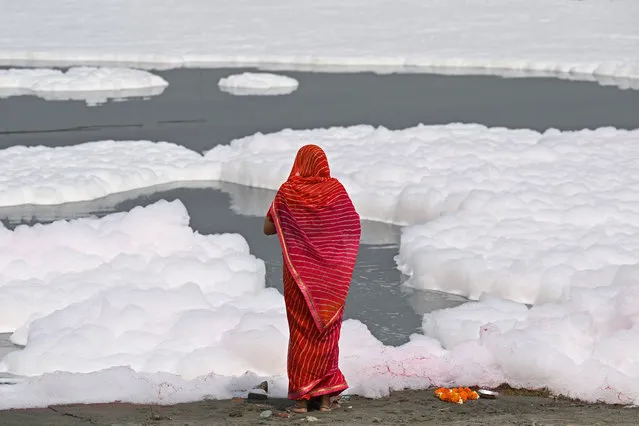 A Hindu devotee offers prayers on the banks of river Yamuna coated with polluted foam in New Delhi on March 21, 2023. (Photo by Sajjad Hussain/AFP Photo)