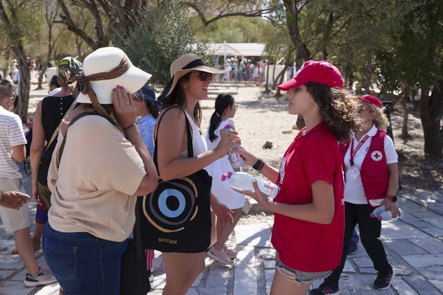 A Red Cross volunteer gives water to tourists at the foot of the Acropolis hill during a hot, windy day in Athens, Wednesday, July 17, 2024. Greece's Culture Ministry ordered the Acropolis closed for several hours in the middle of the day Wednesday, while authorities warned of extreme heat conditions across much of the country. (Photo by Petros Giannakouris/AP Photo)