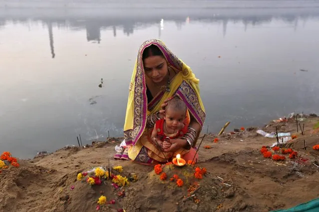 A Hindu woman and her child worship on the banks of river Sabarmati after offering prayers to the Sun god Surya during the Hindu religious festival of Chatt Puja in Ahmedabad, India, November 17, 2015. (Photo by Amit Dave/Reuters)