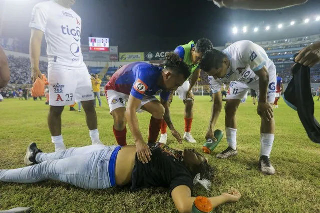 Soccer players attend a fan lying on the field of the Cuscatlan stadium in San Salvador, El Salvador, Saturday, May 20, 2023. At least nine people were killed and dozens more injured when stampeding fans pushed through one of the access gates at a quarterfinal Salvadoran league soccer match between Alianza and FAS. (Photo by Milton Flores/AP Photo)
