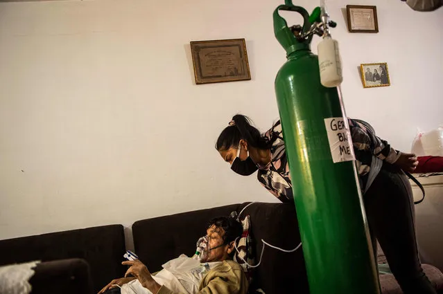 German Blanco's daughter July, 30, checks on her father as he lies on a couch in the living room connected to an oxygen tank at his home in Callao, Peru on February 4, 2021. In Peru, with a population of 33 million and more than 1.14 million people infected, daily deaths duplicated to more than a hundred at the end of January. Since May, the country has been facing a shortage of medical oxygen which has led hundreds of inhabitants to queue for up to 72 hours, sleeping in the streets, to buy this gas which the government has declared a “strategic resource”. (Photo by Ernesto Benavides/AFP Photo)