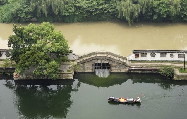 A person rows a boat on a clear river next to a flooded canal at a park in Shaoxing, Zhejiang province, July 7, 2014. (Photo by Reuters/China Daily)