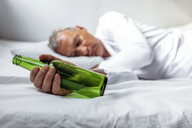 After drinking. Drunk mature man lying on the bed and sleeping after drinking lots of alcohol, Empty bottle in his hand, alcoholism, alcohol addiction and people concept. (Photo by ljubaphoto/Getty Images)