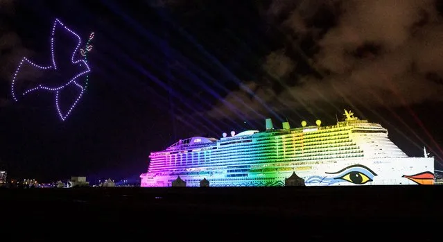 250 drones fly in formation to depict a peace dove (L) as colored lights illuminate the LNG-run cruise ship “AIDAcosma” during its christening ceremony at the “Steinwerder” cruise terminal in the harbour of Hamburg, on April 9, 2022. With 183,900 gross tons and a capacity of 5,200 guests, LNG-run AIDAcosma is the largest cruise ship in the AIDA Cruises fleet. AIDAcosma is the sister ship of AIDAnova, which was the first ship in the world to use the Liquefied natural gas (LNG) drive system. (Photo by Axel Heimken/AFP Photo)
