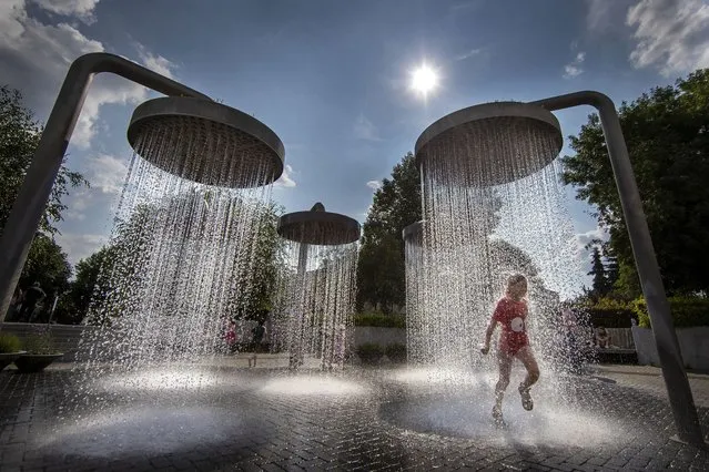A girl cools off in a public fountain in Vilnius, Lithuania, Wednesday, June 21, 2023. The heat wave continues in Lithuania as temperatures have been raising to as high as 32 degrees Celsius (89.6 degrees Fahrenheit). (Photo by Mindaugas Kulbis/AP Photo)