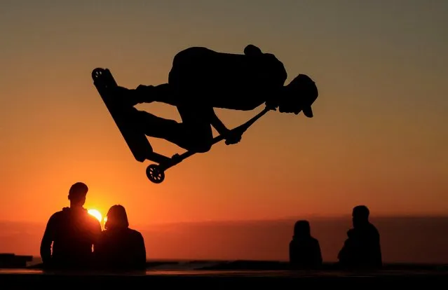 A young man performs a trick on a scooter during the sunset at a skate park on the sea wall of Calais, France on August 15, 2023. (Photo by Pascal Rossignol/Reuters)