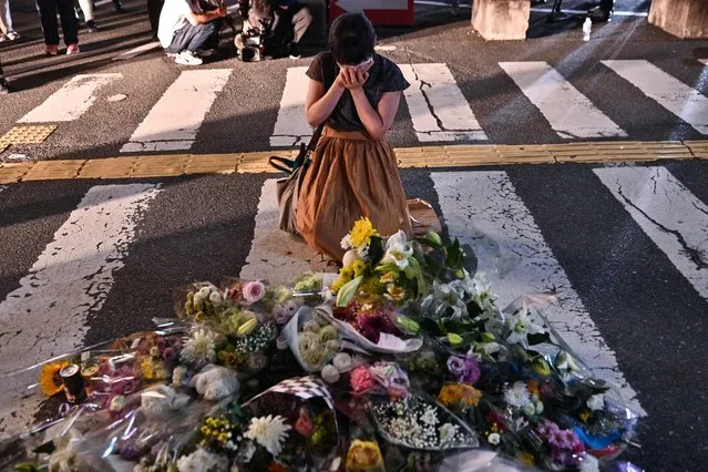 A woman reacts in front of a makeshift memorial where people place flowers at the scene outside Yamato-Saidaiji Station in Nara where former Japanese prime minister Shinzo Abe was shot earlier in the day on July 8, 2022. Abe was pronounced dead on July 8, the hospital treating him confirmed, after he was shot at a campaign event in the city of Nara. (Photo by Philip Fong/AFP Photo)
