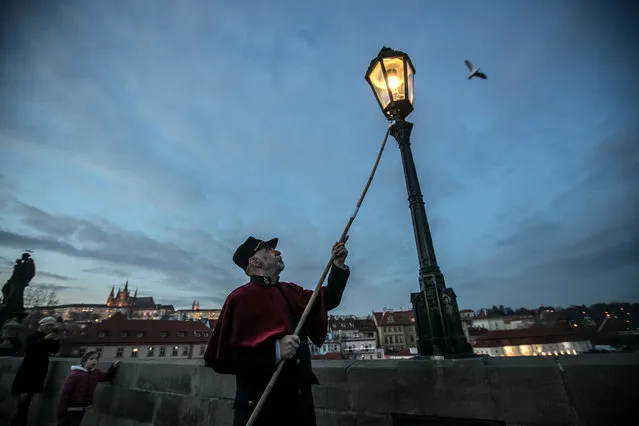 Lamplighter Jan Tater lights a historic gas lamp on Charles Bridge in Prague, Czech Republic, 18 December 2018. Every day at dusk since the end of November and during Advent, Jan Tater and his colleague light 37 historic gas lamps on the medieval Charles Bridge as an attraction for tourists. The first gas lamps on the Charles Bridge were installed in 1848. (Photo by Martin Divisek/EPA/EFE)