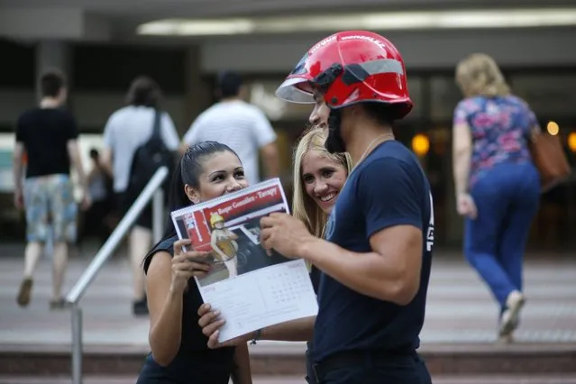In this January 13, 2019 photo, firefighter Daniel Rodriguez sells calendars to a couple of women in Asuncion, Paraguay. Firefighters in the town of San Roque Gonzalez launched a campaign to sell calendars featuring nude pictures of themselves, to help fund their fire station. (Photo by Jorge Saenz/AP Photo)