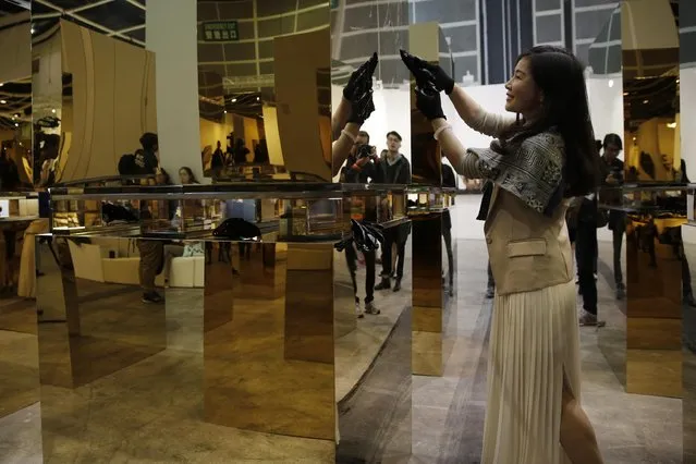 A woman using a black crystal fragment scratches onto the surface of the “18 Cubes” installation created by Chinese artist Zhang Ding during the VIP preview of the art fair “Art Basel” in Hong Kong, Tuesday, March 22, 2016. Ding attracted curious visitors with his “18 Cubes” installation, which consists of 18 large steel boxes plated with 24-karat gold to give them a mirror-like finish. In a twist, Zhang invited fairgoers to scratch whatever they wanted onto the surface, using anything they are carrying with them, or black crystal shards provided for the purpose. (Photo by Kin Cheung/AP Photo)