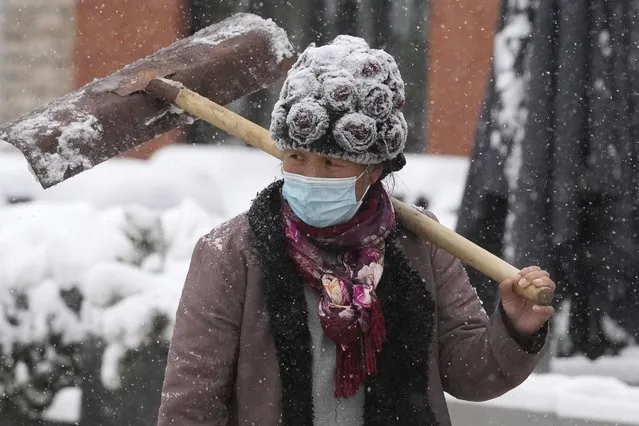 A worker walks with a shovel as fresh snow falls in Beijing, China, Sunday, November 7, 2021. An early-season snowstorm has blanketed much of northern China including the capital Beijing, prompting road closures and flight cancellations. (Photo by Ng Han Guan/AP Photo)