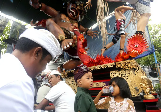 Balinese people sit in front of a giant effigy locally known as “ogoh-ogoh” that represents evil spirits to celebrate Nyepi, the annual day of silence marking Balinese Hindu new year in Bali, Indonesia, Wednesday, March 6, 2019. (Photo by Firdia Lisnawati/AP Photo)