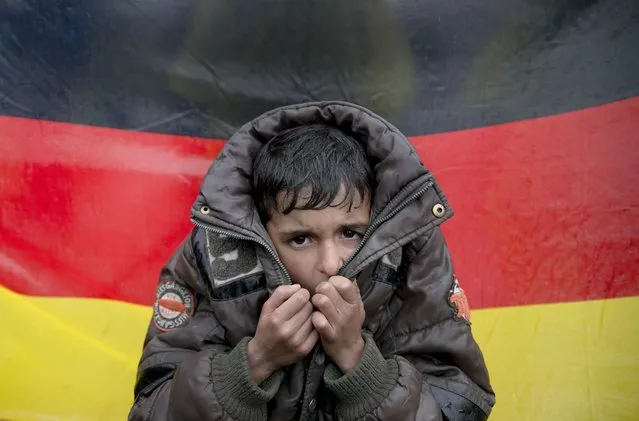 A child tries to warm his hands, backdropped by Germany's flag as protesting migrants stage a sit in protest on the railway tracks at northern Greek border station of Idomeni, Wednesday, March 9, 2016. (Photo by Vadim Ghirda/AP Photo)