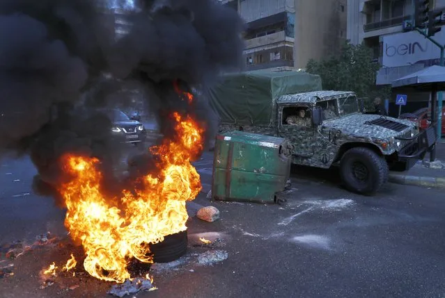 Army soldiers in a military vehicle pass by burning tires lit by protesters during a protest against the increasing prices of consumer goods and the crash of local currency in Beirut, Lebanon, Monday, November 29, 2021. (Photo by Hussein Malla/AP Photo)