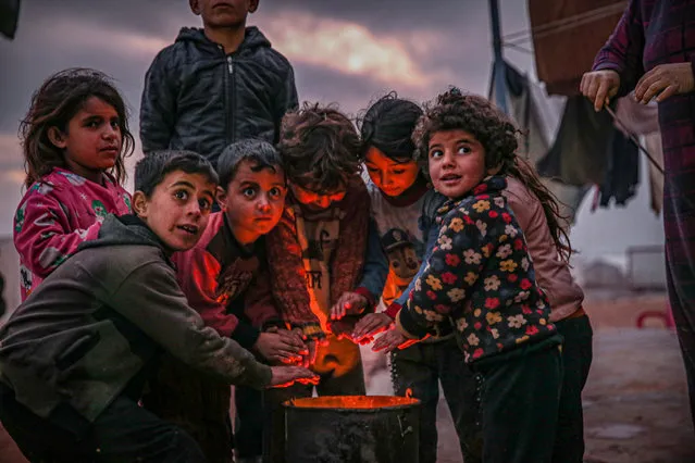 Syrian kids try to get warm around fire near their makeshift tentas rain and cold weather, which was effective tents in Kafr Lusin district where infrastructure services were insufficient, made the lives of the residents difficult during winter season in northern Idlib, Syria on January 31, 2021. (Photo by Muhammed Said/Anadolu Agency via Getty Images)
