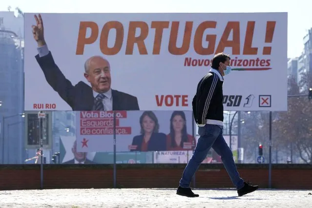 A man wearing a face mask walks past election campaign billboards in Lisbon, Thursday, January 20, 2022. Portugal's government is under fire over its preparations for people infected with COVID-19 to vote in an upcoming snap election, as officials struggle to square the constitutional right to vote with a duty of care for public health. Eligible voters who are infected and confined at home - as many as 600,000 people on the day of the Jan. 30 election, officials estimate – are to be allowed to go to polling stations as an exceptional measure, the government announced Thursday. (Photo by Armando Franca/AP Photo)