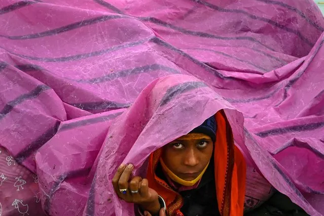 A boy uses a plastic sheet to shelter from rain at the Gangasagar Mela on the occasion of Makar Sankranti, a day considered to be of great religious significance in Hindu mythology, at Sagar Island, around 150 kms south of Kolkata on January 14, 2022. (Photo by Dibyangshu Sarkar/AFP Photo)