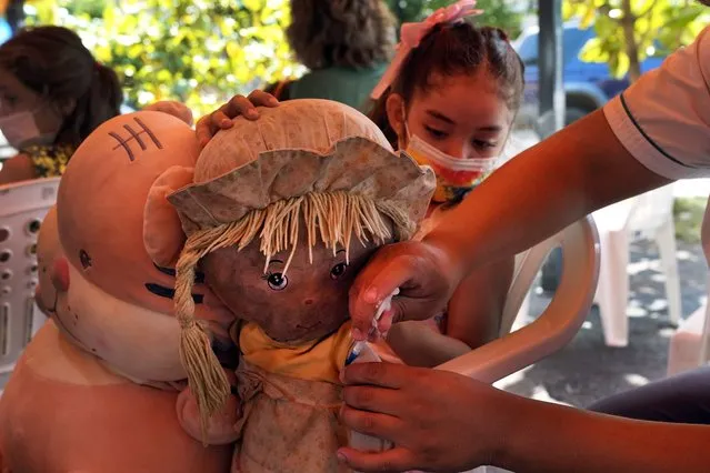 A health worker pretends to give a shot to a girl's doll to help put her at ease before giving her a shot of the Coronavac vaccine for COVID-19, at a sports center as children age 5 – 11 start getting vaccinated in Asuncion, Paraguay, Monday, January 31, 2022. (Photo by Jorge Saenz/AP Photo)