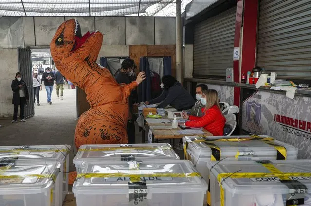 A person dressed in a dinosaur costume votes on the second day of the Constitutional Convention election to select assembly members that will draft a new constitution, in Santiago, Chile, Sunday, May 16, 2021. Chileans favored left-leaning independent candidates in electing an assembly that will draft a new constitution, replacing the one imposed in the 1980s during the military dictatorship. (Photo by Esteban Felix/AP Photo)