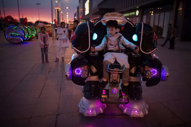 A boy rides a robot style vehicle outside a shopping mall in Daqing, Heilongjiang province, China on May 2, 2016. (Photo by Nicolas Asfouri/AFP Photo)