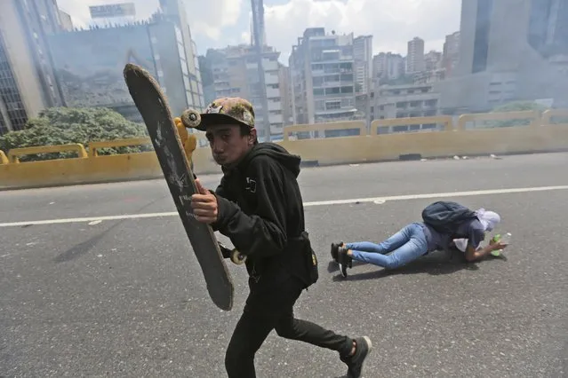 Demonstrators take cover of tear gas fired by Bolivarian National Police during a protest in Caracas, Venezuela, Thursday, April 6, 2017. Tens of thousands of demonstrators shut down Venezuela's capital blocking the city's main artery to protest what they call an attempted coup by the socialist administration. (Photo by Fernando Llano/AP Photo)