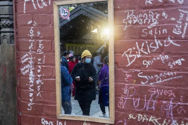 Nepalese devotees are reflected on a mirror on a wall of a Saraswati temple, on which children have written their names during Shri Panchami festival in Kathmandu, Nepal, Sunday, February 6, 2022. (Photo by Niranjan Shrestha/AP Photo)