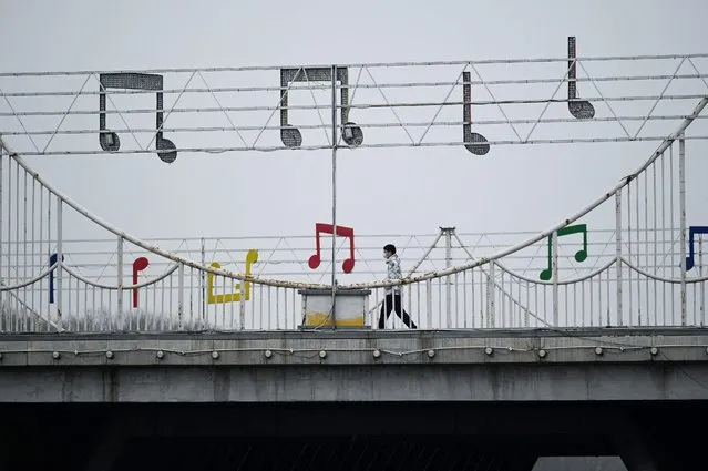 A man walks across a bridge decorated with musical note symbols in Beijing on March 29, 2022. (Photo by Wang Zhao/AFP Photo)