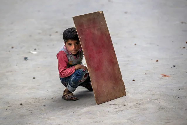 A Kashmiri boy shields himself with plywood from stones and glass marbles during a clash between Indian policemen and protesters during a protest in Srinagar, Indian controlled Kashmir, Friday, May 19, 2017. Government forces fired tear gas during clashes with Kashmiri protesters in the Indian-controlled portion of Kashmir after Friday prayers called by separatist leaders against the continuous detention of woman separatist leader Asiya Adrabi, chairman of Dukhtaran-e-Millat, or Daughters of the Nation. They also demand release of all political prisoners from Indian prisons. (Photo by Dar Yasin/AP Photo)